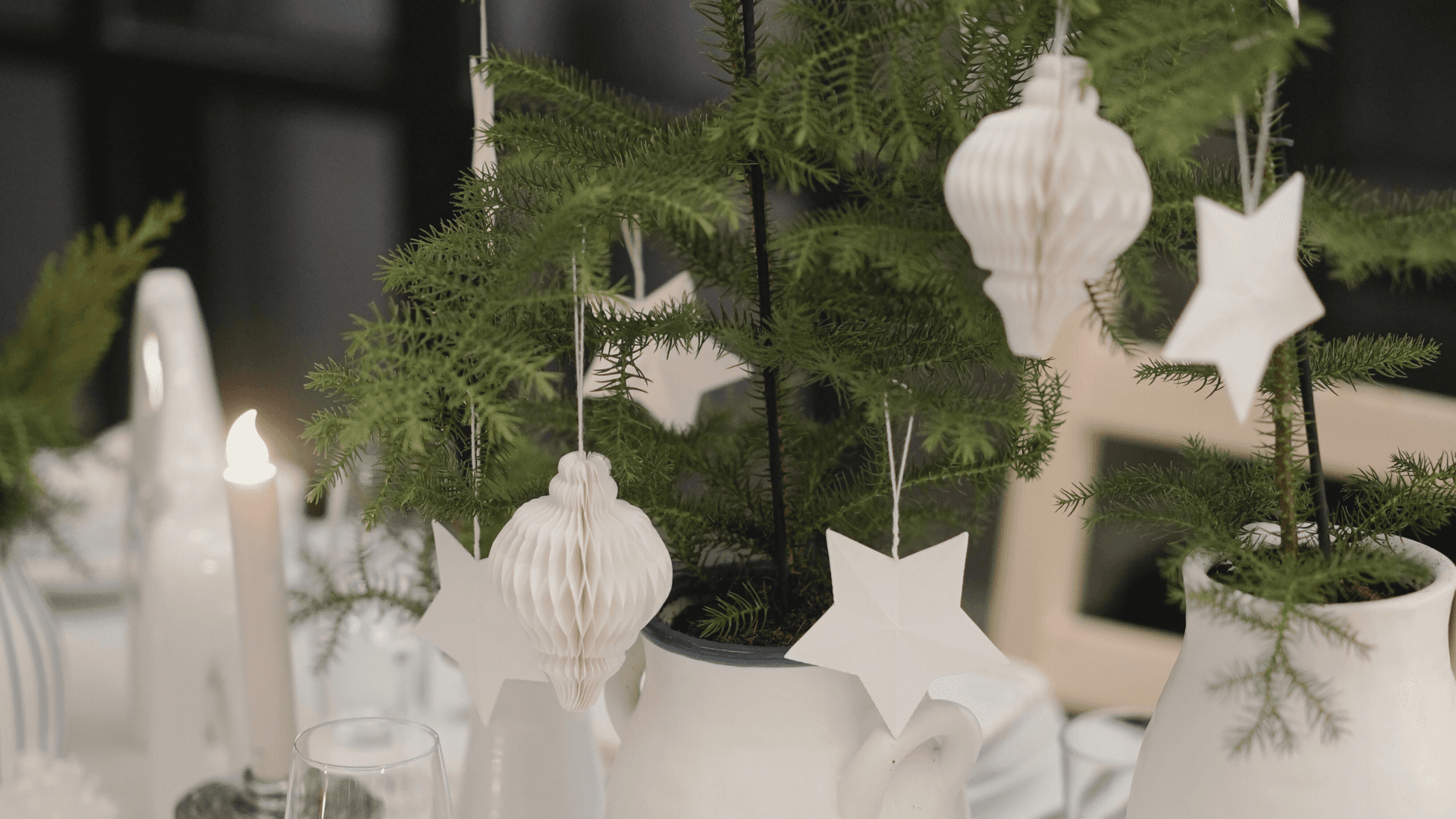 Small Scandinavian tabletop tree decorated with white paper ornaments and stars on a minimal holiday table setting.