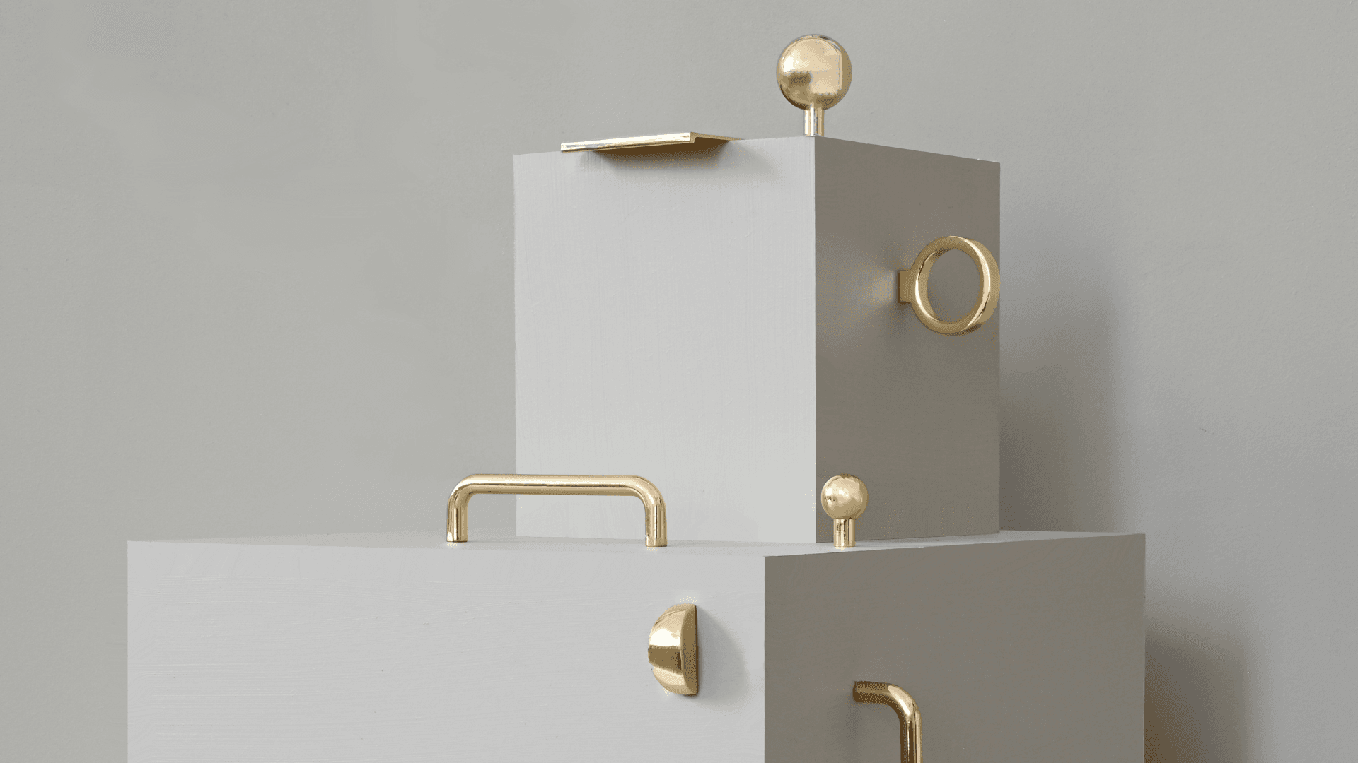 Selection of brass cabinet handles and knobs by Prettypegs displayed on minimalist grey blocks.
