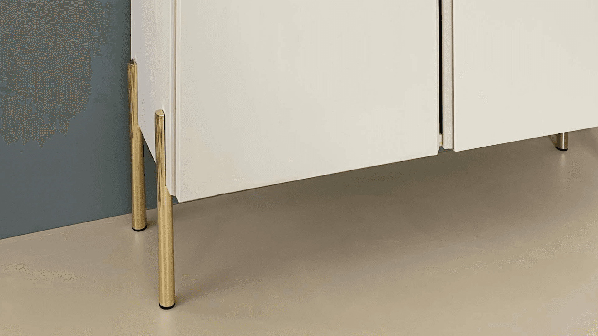 Modern white cabinet with slim Prettypegs brass legs against blue wall.