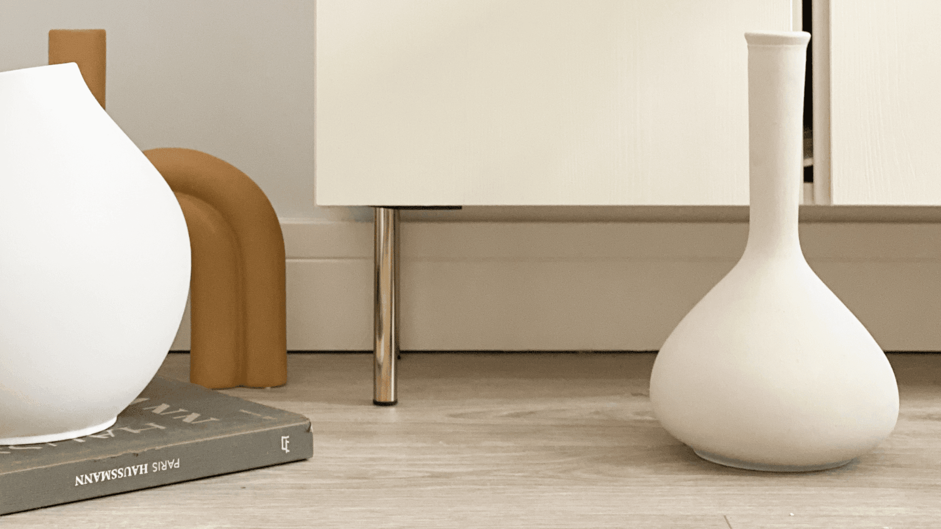 Close-up of brass furniture legs on cabinet styled with minimalist Scandinavian decor and ceramic vases.
