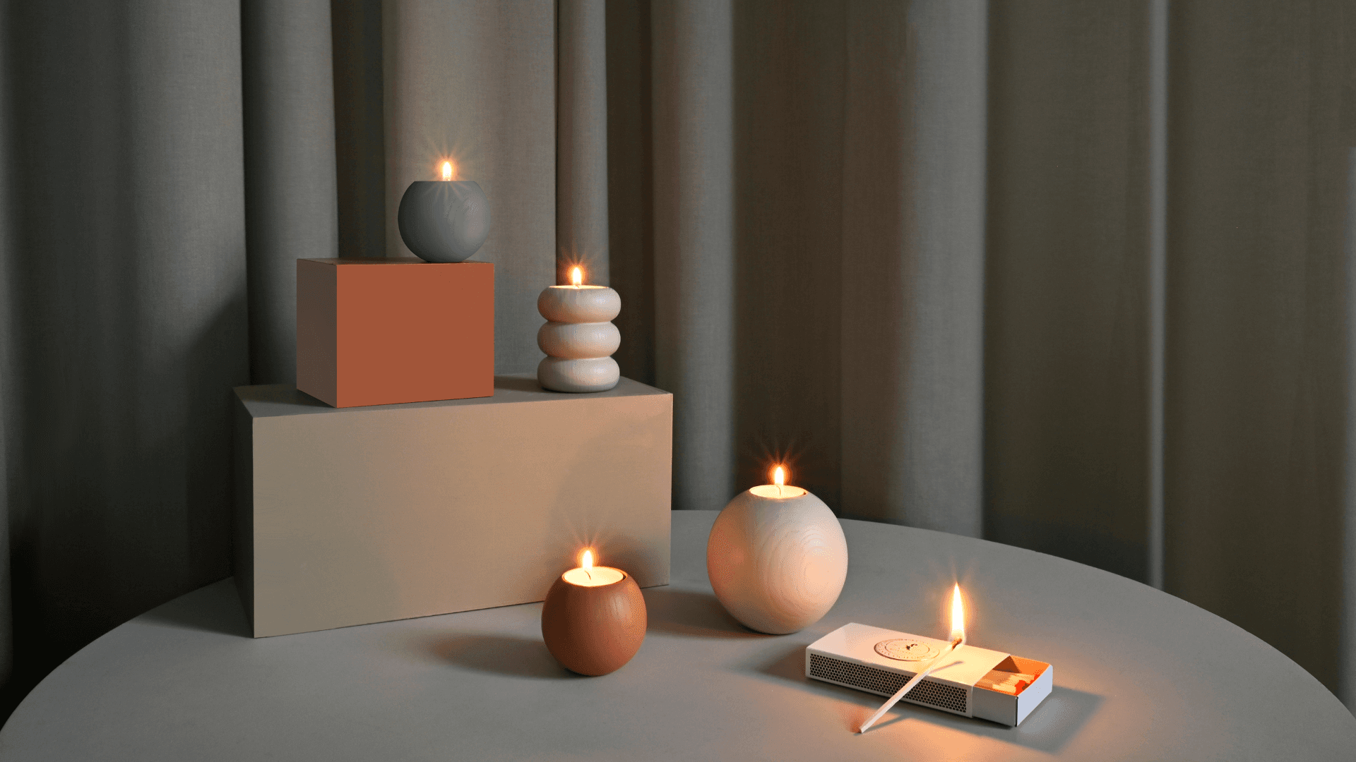 Minimalist candle arrangement with soft warm light, styled on neutral blocks in a Scandinavian-inspired setting.